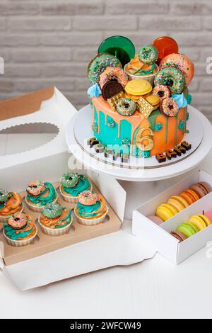Delicious two-sided birthday cake made in green and orange colors richly decorated with donuts and lollipops. Celebrating two birthdays at once. Stock Photo
