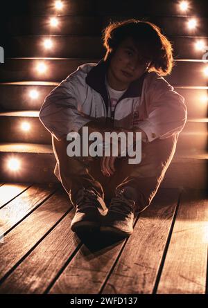 Man sitting on steps at night, illuminated by overhead light Stock Photo