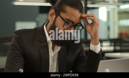Thoughtful sad worried anxious hard decision problem tired headache Arabian business man thinking online trouble work male pensive manager working on Stock Photo