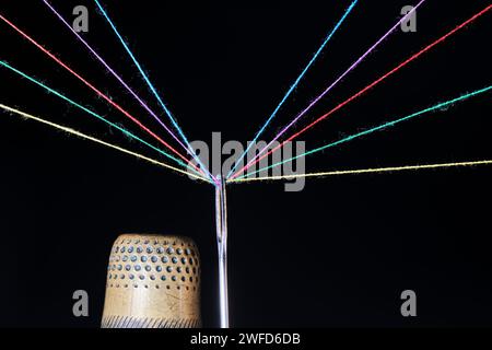 Thimble, eye sewing needle and multicolored threads passed through it black background Stock Photo