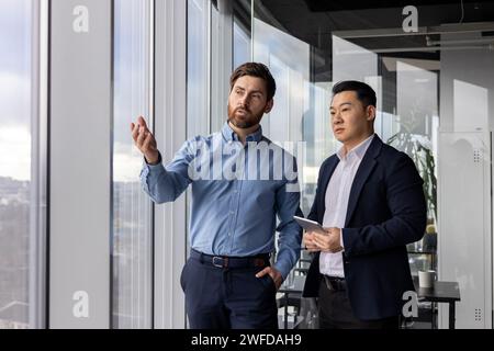Two male corporate professionals engage in a serious discussion about business strategies in their well-lit office. Stock Photo