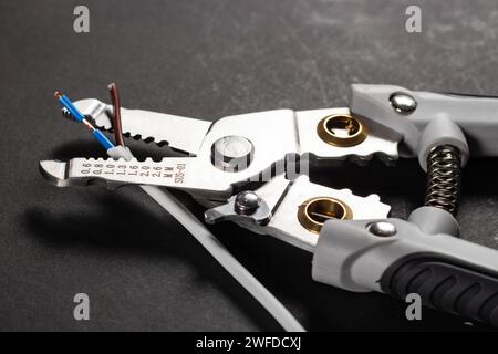 Removing the insulation from the conductor using a tool. Wire stripping tool on dark background. Stock Photo