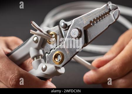 An electrician wearing gray work gloves is stripping electrical wires with a stripper Stock Photo