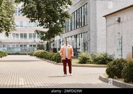 cheerful indian blind man in orange jacket with glasses and walking stick taking walk in park Stock Photo