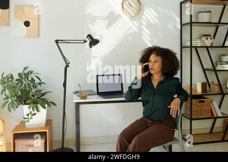 Software developer sitting at her home office desk and talking on phone Stock Photo