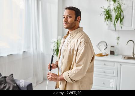 handsome blind indian man in comfortable homewear using walking stick while at home, disabled Stock Photo
