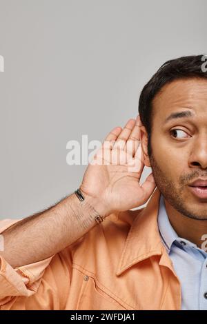 curious indian male model in bright orange jacket overhearing something on gray background Stock Photo