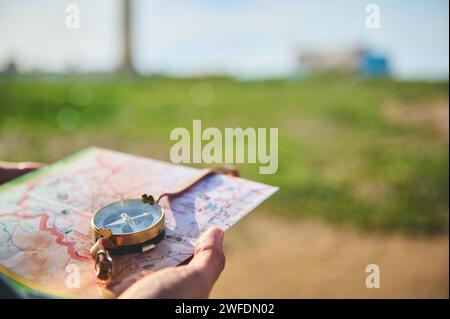 Close-up tourist's hand holds a compass with magnetic arrow showing north direction, over a map against lighthouse background. Copy advertising space. Stock Photo