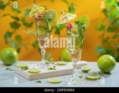 Two cocktails in long glass filled with ice and lemon slices garnished with small yellow umbrellas, cherries and lemon slices on a wooden board agains Stock Photo