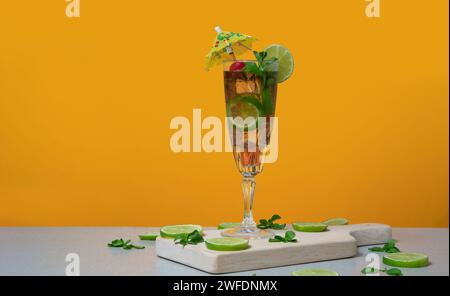 Cocktail in long glass filled with ice and lemon slices garnished with small yellow umbrellas, cherries and lemon slices on a wooden board against ora Stock Photo