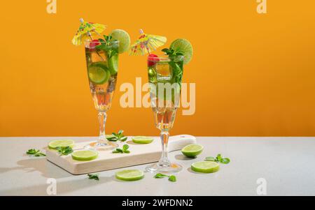 Two cocktails in long glass filled with ice and lemon slices garnished with small yellow umbrellas, cherries and lemon slices on a wooden board agains Stock Photo