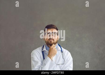 Portrait of a dreamy young male doctor with a pensive expression on a gray background. Stock Photo
