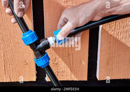 Connecting fittings for plastic pipes with threaded compression clamp, plumber tightens nut on tee splitter when installing drinking and irrigation Stock Photo