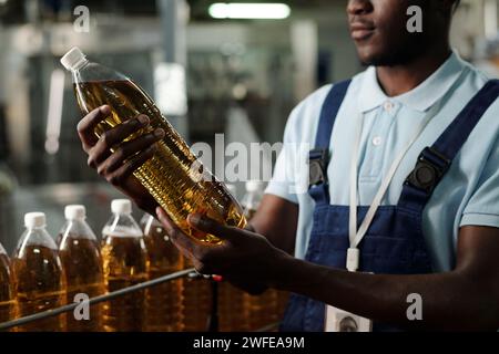 Young African American inspector of quality control holding capped plastic bottle with fizzy soda or lemonade while working at factory Stock Photo
