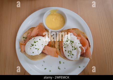Two poached eggs on smoked salmon and an english muffin. A small dish of hollandaise sauce is on the side. Stock Photo