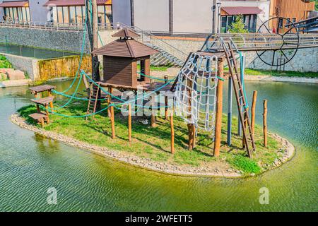 Colorful children's play activities in a public park surrounded by green pond at sunset Kids run, slides, swings on a modern playground. Urban neighbo Stock Photo