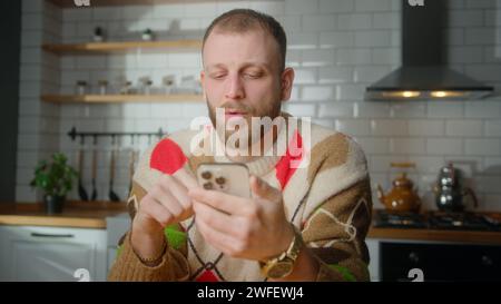 Man sit in kitchen surfing internet on mobile phone, checking email, reading media news, scrolling social medias, using mobile applications on smartph Stock Photo