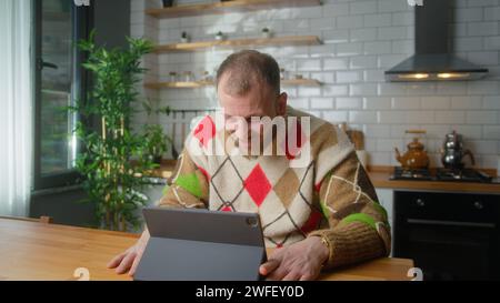 Smiling man sitting in the kitchen having video call conversation through tablet computer. Share news, talk to family, enjoy webchat virtual meeting Stock Photo