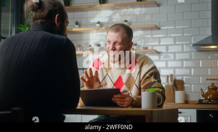 Two co-worker are sitting in the kitchen having a fun chat and laughing. Man using tablet, taking a coffee break at work, technology company workers, Stock Photo