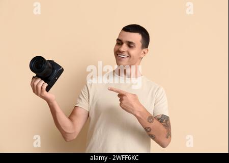Male photographer pointing at modern camera on beige background Stock Photo