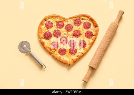 Tasty heart shaped pizza with rolling pin and cutter on yellow background Stock Photo