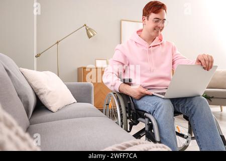 Young man in wheelchair with laptop at home Stock Photo