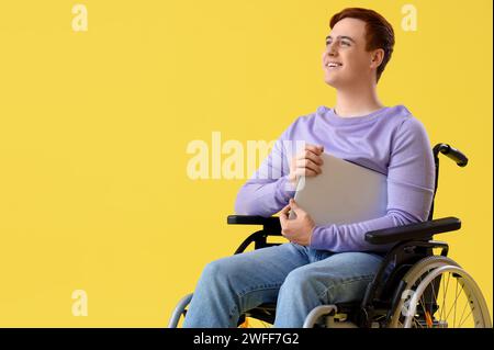 Young man in wheelchair with laptop on yellow background Stock Photo