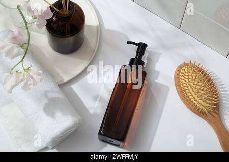 A wooden brush and pump bottle without label displayed on white background. A round dish with flower vase, reed diffusers and a towel arranged on. Moc Stock Photo