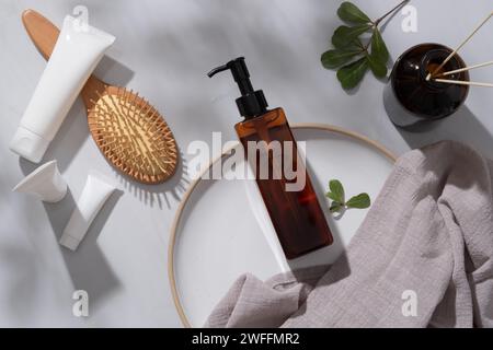 An empty label pump bottle putted on a round dish, tubes with different sizes, a wooden brush and reed diffusers displayed. Skincare product concept Stock Photo