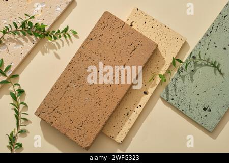 Several stone podiums with different color are arranged on a beige background. Decorated with green leaves. Blank space to promote product Stock Photo