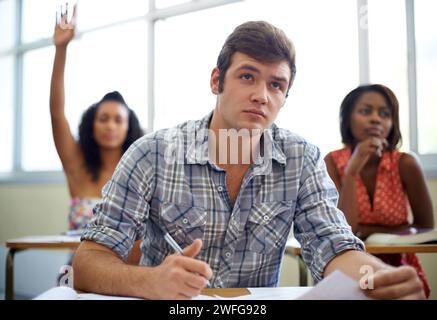 Students, questions and learning in classroom for education, language development and knowledge in high school. Young people raise hands at desk for Stock Photo