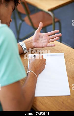 Student, writing and cheating in exam with hands for answers, math solution or knowledge in classroom. Person or liar with test paper, wrong formula Stock Photo