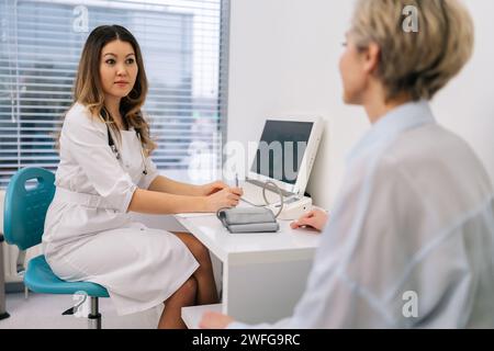 Serious female physician talk to unrecognizable middle-aged woman patient at appointment in hospital. Client listens professional cardiologist advices Stock Photo