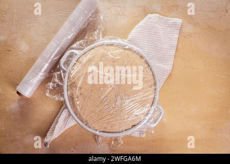 Yeast dough covered by plastic wrap, proofed dough for baking bread or pizza Stock Photo