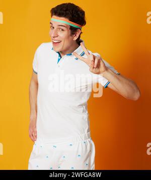 Portrait, tennis and man with peace sign, smile and confident guy on a yellow studio background. Person, athlete and model with v gesture and symbol Stock Photo