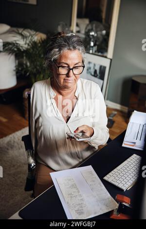 Businesswoman with disability photographing documents while sitting at desk in home office Stock Photo