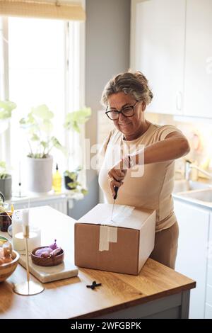 Woman with disability opening package using knife while standing in kitchen at home Stock Photo