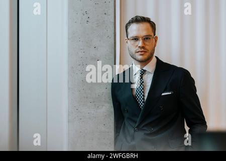 Portrait of confident young businessman leaning on column in corporate office Stock Photo