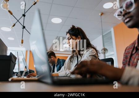 Young businesswoman using laptop while working amidst colleagues at desk in creative office Stock Photo