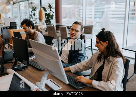 Young male and female colleagues discussing over computer while sitting by businessman at desk in office Stock Photo