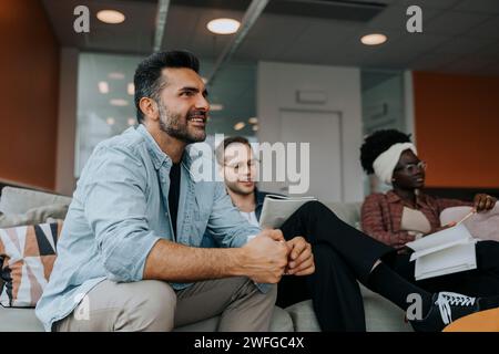 Happy mature businessman sitting by young colleagues sitting on sofa during conference meeting Stock Photo