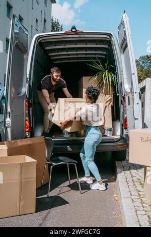 Multiracial couple unloading cardboard boxes from van trunk Stock Photo