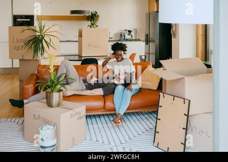 Happy multiracial couple having fun while sitting on sofa in living room at new home Stock Photo