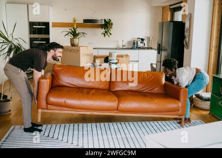 Happy multiracial couple keeping sofa on carpet in living room at new home Stock Photo