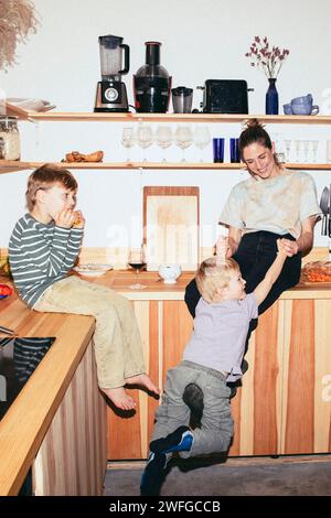 Happy woman playing with son while sitting on kitchen counter at home Stock Photo