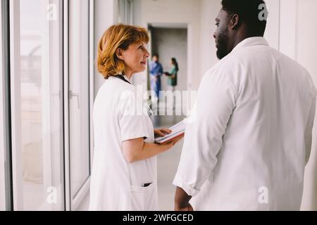 Senior female doctor discussing with male colleague in corridor at hospital Stock Photo