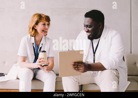 Cheerful male and female doctors sitting on sofa at hospital Stock Photo