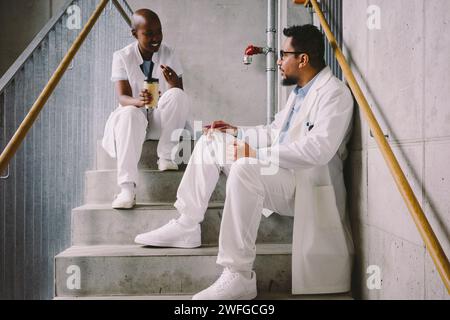 Happy medical colleagues talking while sitting at staircase during coffee break Stock Photo
