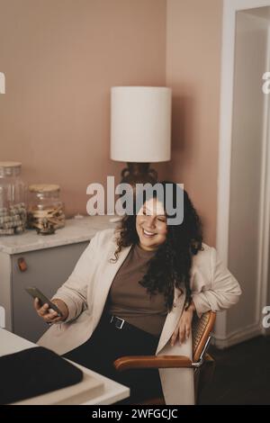 Smiling businesswoman holding smart phone while sitting on chair at office Stock Photo