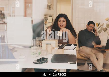 Businesswoman talking with colleague sitting at office seen through glass window Stock Photo
